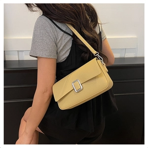 Detail view of mustard yellow pebbled leather shoulder bag with silver buckle on a model
