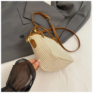 Close-up of beige woven straw bucket bag with brown leather trim and gold hardware detail