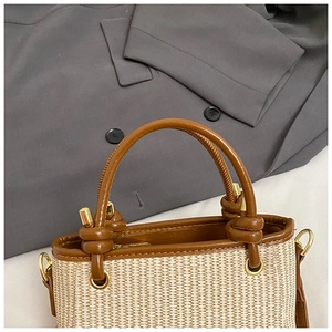 Detail of woven straw handbag with brown leather handle and gold hardware accents