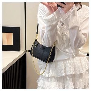 Detail showing black embossed leather texture and gold chain strap of the shoulder bag