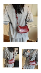 Detail of burgundy leather half-moon bag with knotted strap and silver orb charm pendant