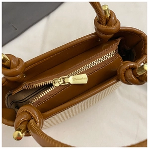 Detail view of woven straw handbag featuring knotted handle and gold sphere metal buckle