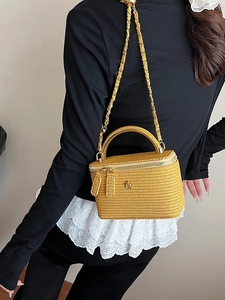 Yellow woven vanity bag with chain strap and camellia logo shown on a female model
