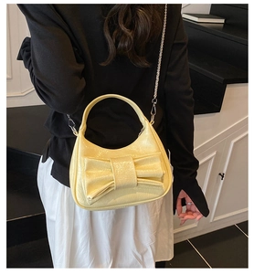 Close-up of a pale yellow bow bucket bag with shiny patent finish and silver chain strap