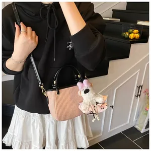 Detail of pink woven straw crossbody bag with black leather straps and plush bear charm