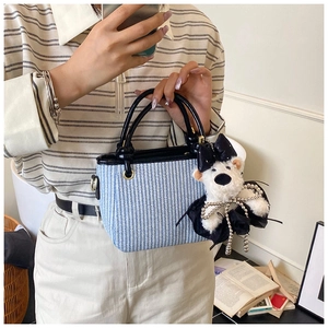 Detail of blue and white woven handbag with leather handles and plush bear charm