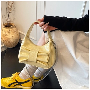 Close-up of yellow bow detail on a wrinkled patent leather bucket bag with chain strap
