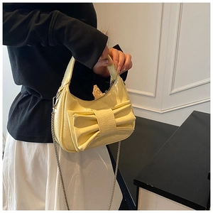 Detail of light yellow bow-tie shoulder bag with pleated patent leather and chain strap