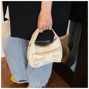 Detail of cream bow bucket bag with glossy pleated texture and top handle design