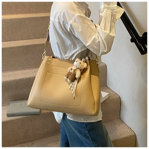 Close-up of beige tote bag with a plush bear charm and decorative front pocket