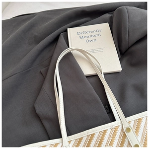 Detail of striped woven tote bag with slim white shoulder straps on elegant dark blazer