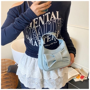 Detail view of light blue patent leather bucket bag with large bow and metal chain strap
