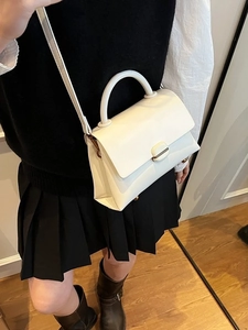 Minimalist white leather tote bag with oval buckle and top handle in a lifestyle setting