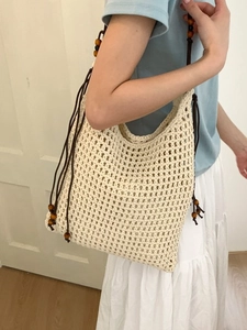 Sac seau tissé beige minimaliste avec perles en bois sur mannequin pour vacances à la plage