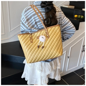 Detail of striped straw tote bag featuring brown leather straps and a fuzzy charm