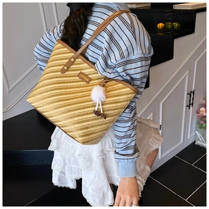 Detail view of woven striped tote bag with brown leather trim and white plush charm accessory