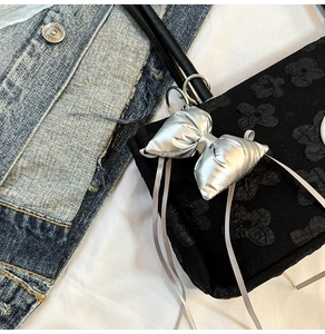Détail du sac sous le bras noir avec texture florale 3D et breloque noeud argenté chic