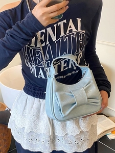 Light blue bow bucket bag with pleated texture and silver chain strap shown by a model