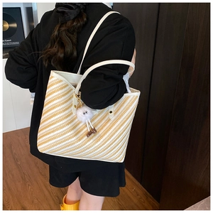 Detail of yellow and white striped woven tote bag with a white plush charm accessory