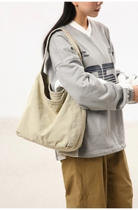 Side view of a large khaki canvas tote bag worn by a model in a minimalist setting