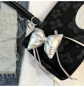 Détail d'un nœud argenté sur un sac noir avec motif floral 3D et texture gaufrée