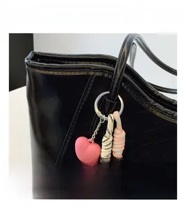 Detail shot of black leather tote bag featuring pink heart charm and braided tassels