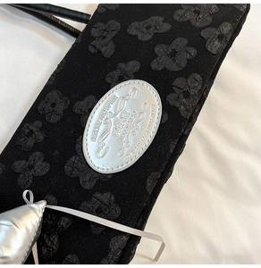 Détail du tissu jacquard floral noir avec une étiquette de marque argentée sur le sac