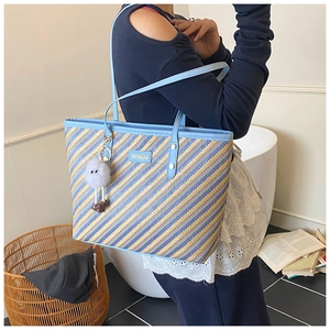Detail of striped woven tote bag with light blue leather trim and plush charm