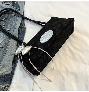 Détail du sac bandoulière en jacquard noir avec plaque ovale et breloque en cœur
