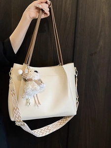 Beige leather tote bag with a wide patterned strap and a plush sheep charm pendant
