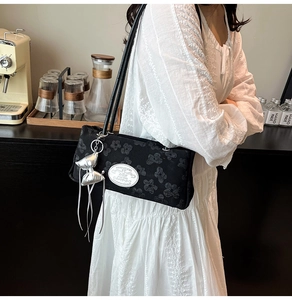 Détail du sac porté épaule en jacquard noir avec breloque nœud argenté et plaque