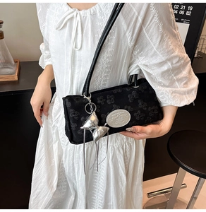 Détail d'un sac d'épaule noir texturé avec charm nœud argenté et étiquette en métal