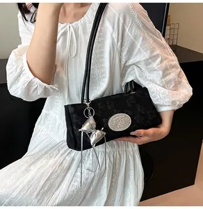 Détail du sac sous le bras noir gaufré avec breloque nœud argenté et plaque logo
