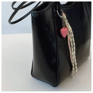 Detail view of smooth black leather tote bag with a pink heart charm and braided strap