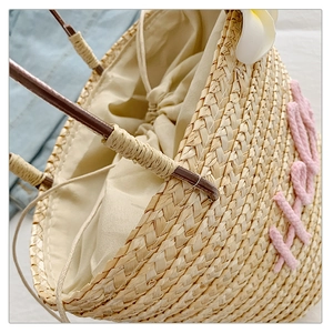 Close-up of beige straw bucket bag featuring pink Hello embroidery and a plumeria flower