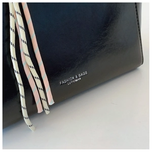 Detail of black leather tote showing contrast woven lanyards and silver fashion text