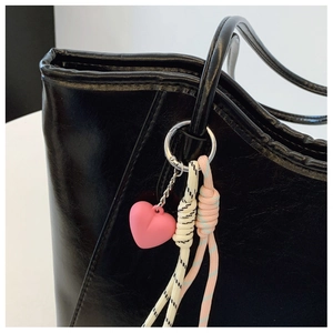 Detail of pink heart keychain charm with striped woven ropes on a black leather tote bag