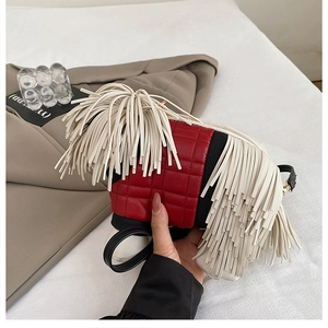 Detail of red quilted crossbody bag featuring long white fringe and black strap