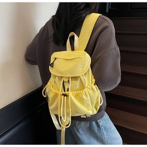 Detail of lemon yellow pleated nylon backpack with flap closure and drawstring side pockets