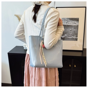 Light blue tote bag with heart charm and woven tassel shown on a model's shoulder