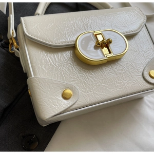 Détail de la texture en cuir verni blanc plissé et fermoir doré sur le sac