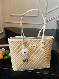 Large striped woven tote bag in yellow and white with a plush monster bag charm