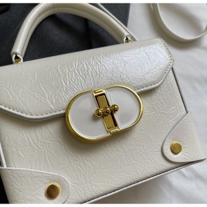 Détail d'un sac bandoulière blanc avec texture froissée et fermoir doré ovale élégant