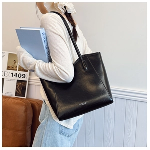 Detail of minimalist black faux leather tote bag with slim shoulder straps and logo