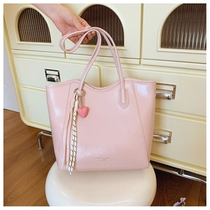 Pink glossy tote bag with heart pendant and tassel shown in a casual lifestyle setting