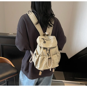 Close-up of beige nylon backpack featuring drawstring pockets and modern fold-over flap design