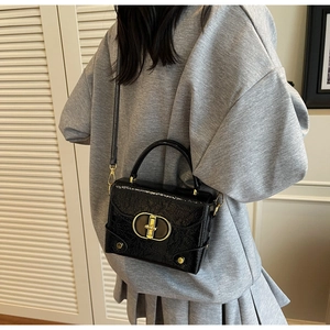 Détail d'un sac bandoulière en cuir verni noir avec un fermoir ovale en métal doré