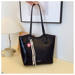 Detail of a large black tote bag with pink heart pendant on a cozy office desk