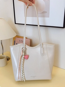 Cream large capacity tote bag with heart charm and woven fringe on beige table