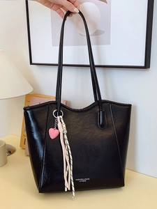 Black large capacity tote bag with long straps and heart charm on an indoor desk